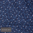 Close-up of a dark Halo blue fabric with a small white and light blue speckled pattern and a stitched seam. A small fabric label at the bottom left reads DUNNING.