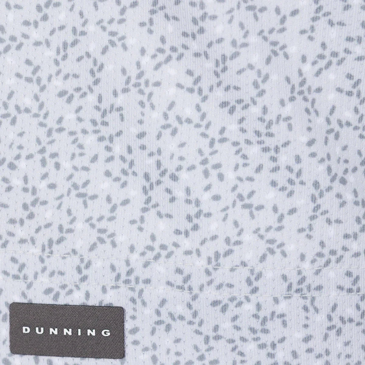 Close-up of a light Micro-Chip gray fabric with a scattered small dark gray leaf-like print and a dark gray DUNNING brand patch at the bottom left.